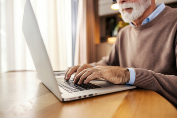 Close up of senior man sitting at home and working remotely on a laptop.