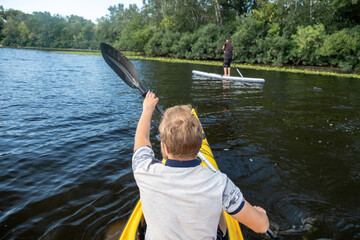 Kayaker paddles gliding towards friend engaging in paddleboarding. Friends have rest immersed in water sport activities on vacation