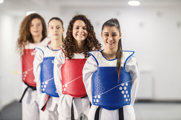 Taekwondo athletes standing in a row wearing doboks and smiling at the camera.