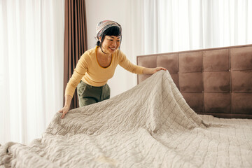Tidy japanese woman is making her bed in a bedroom.
