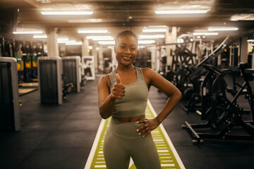 Portrait of a smiling black fit sportswoman in a gym giving thumbs up.
