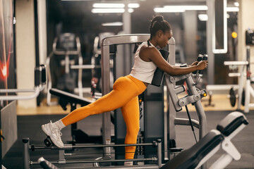 A fit black sportswoman in shape practicing on gluts gym machine.