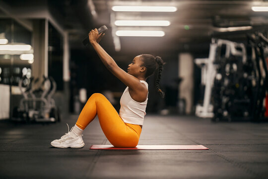 A strong black sportswoman practicing situps with weight plate at the gym.