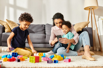 Obraz premium cheerful african american woman in homewear looking at phone while playing with her sons at home