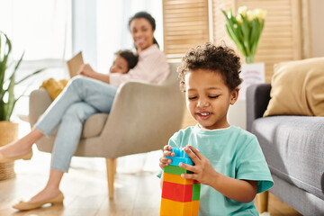 focus on little african american boy playing with toys with his blurred mom and brother on backdrop