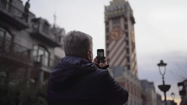 Elderly man travels and uses his smartphone to capture beauty of urban architectural landmarks. 