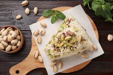 Piece of tasty halva with pistachios and mint on wooden table, flat lay