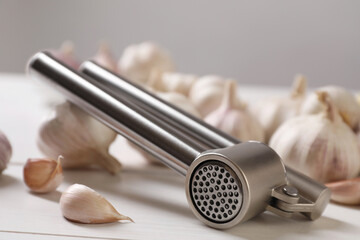 Metal press and garlic on white table, closeup
