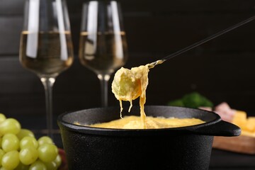 Dipping grape into fondue pot with melted cheese on table, closeup