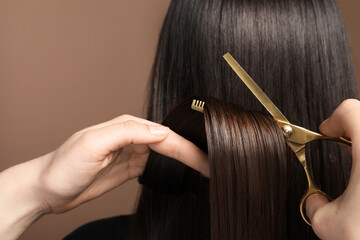 Hairdresser cutting client's hair with scissors on light brown background, closeup