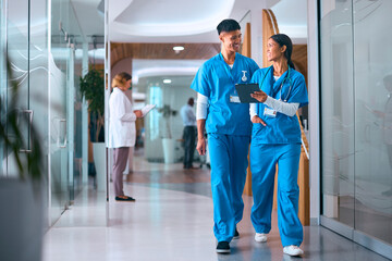 Male And Female Doctors Or Nurses In Scrubs With Digital Tablet In Hospital With Colleagues Behind