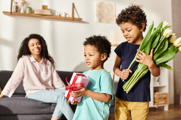 focus on merry african american boys with tulips and gift with their blurred mother on backdrop
