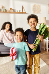 focus on jolly african american brothers with tulips and present with their blurred mom on backdrop