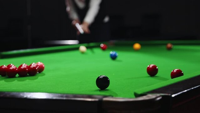 Blurred young man in white shirt playing billiards, snooker game, focusing on shot with cue stick. Concentration and precision. Focus on balls. Billiards sport, gambling, hobby, leisure, game concept