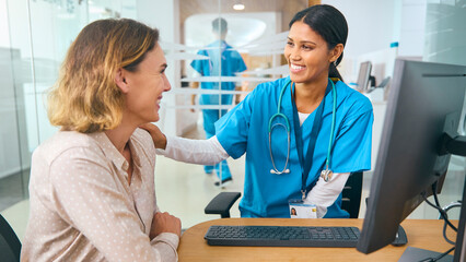 Obraz premium Female Doctor Wearing Scrubs At Hospital Appointment Giving Good News To Woman Patient 