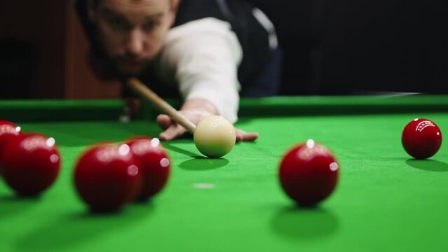 Handsome young man in white shirt playing billiards, snooker game, focusing on shot with cue stick. Concentrated player. Focus on balls. Concept of billiards sport, gambling, hobby, leisure, game