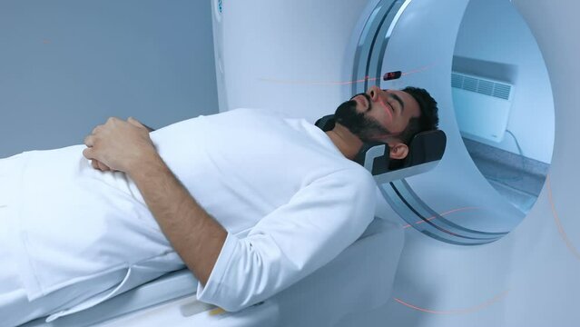 Prevention of cancer diseases and healthcare with new technologies. Male patient lying on CT scanner during machine imaging body, lights up infrared rays and passes through circle.