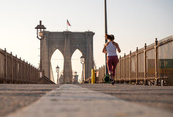 A runner jogging towards the arches of the sunlit Brooklyn bridge.