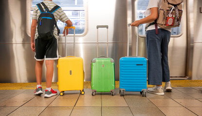 Two travelers with colorful suitcases standing at a subway platform.