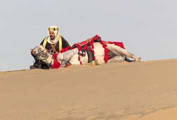 Saudi man in traditional clothing resting with his horse in a desert