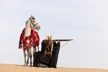Saudi man with his horse in a desert, aiming a riffle