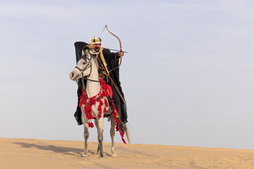 Saudi man in traditional clothing, shooting an arrow, in the desert with a white horse