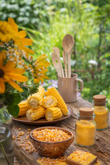 Kolby kukurydzy, ziarna i mąka kukurydziana na drewnianym stole w ogrodzie. - obrazy, fototapety, plakaty