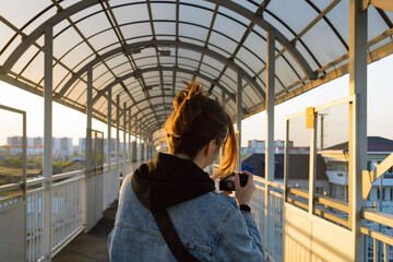 A girl stands on a pedestrian bridge at sunset and takes pictures