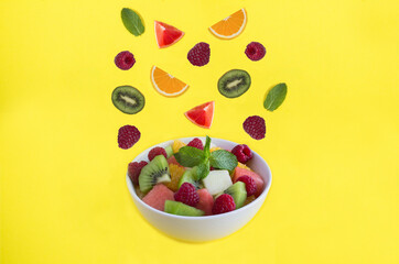 Fruit salad in the white bowl, fruit and berry on the yellow background. Copy space.