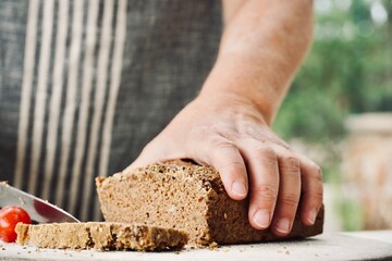 Woman in apron with close-up hands cutting homemade whole wheat bread.