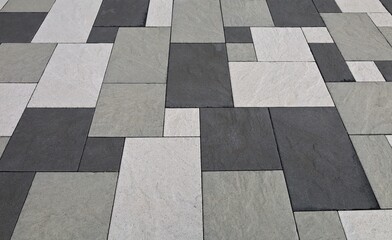 Black, white and gray concrete tiles of different shapes in an outdoor pavement. Background and...