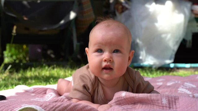 Beautiful caucasian baby 2-3 months lying on stomach on a blanket in  a warm sunny day outdoor with grass. 4k video.