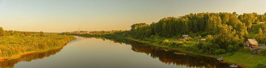 Summer panorama of the river with forest and houses on the shore.