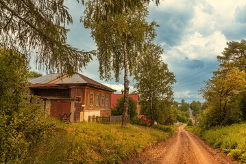 Village houses standing along a dirt road with trees.