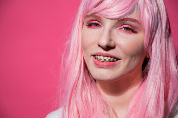 Close-up portrait of a young woman with braces in a pink wig on a pink background.