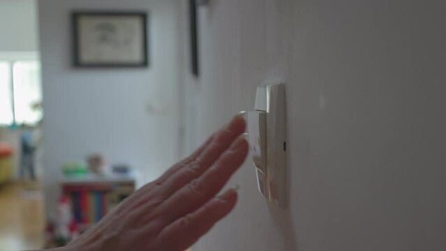 A close-up of a hand flipping a wall light switch in a cozy indoor setting, highlighting everyday routines and home functionality.