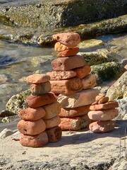 Cairn created with old red clay bricks on beach rocks in sunlight