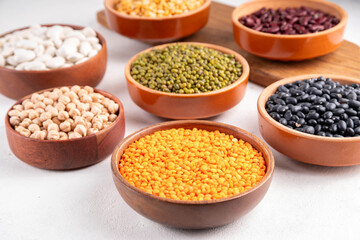 Various dried  beans, lentils, mung, chickpea, pea  assortment in wooden bowls. Legumes on white table top view. Vegan protein sources food, copy space