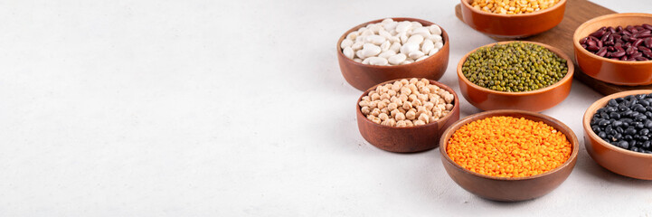 Various dried  beans, lentils, mung, chickpea, pea  assortment in wooden bowls. Legumes on white table top view. Vegan protein sources food, copy space
