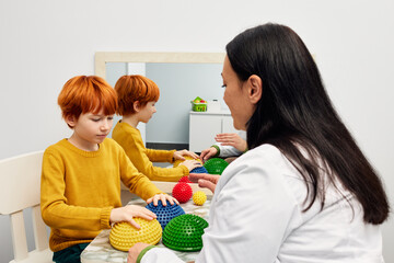 Occupational therapist using sensory integration therapy to improve sensory processing for male child patient. Doctor using hedgehog half balls to develop the boy's fine motor skills