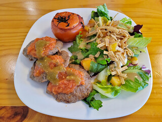 Succulent grilled beef patties topped with salsa, accompanied by a charred tomato and a colorful salad with crispy tortilla strips