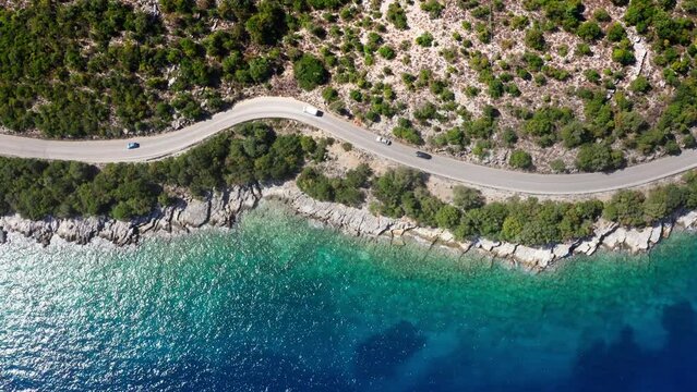 4K Drone footage of casr moving by the sea curved road near a tranquille waves on the Greek coast on Cephalonia island. Transportation, nature concept.