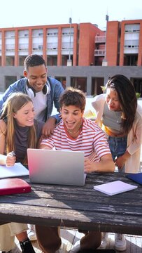 Vertical. Group of multiracial happy teenage students using laptop, working on university assignment homework project at university campus. Meeting of young classmates looking information on computer