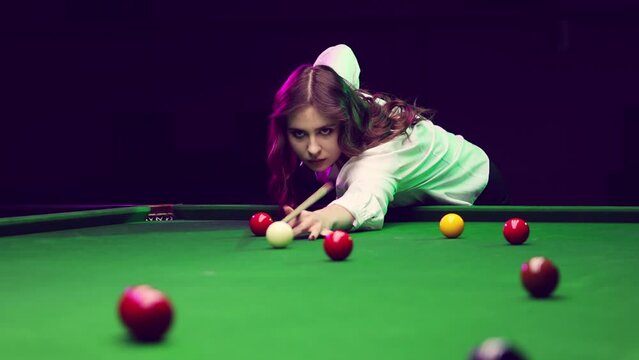 Focused young woman lines up his shot on the billiards table, showcasing precision and skill. Promotion of local billiards tournament. Concept of billiards sport, gambling, hobby, leisure, game