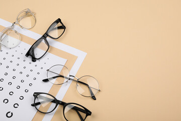 Vision test chart and glasses on beige background, flat lay. Space for text