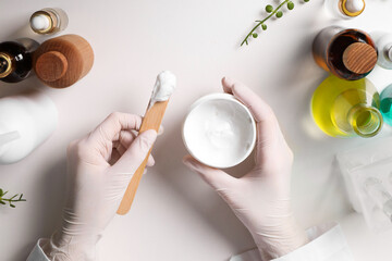 Dermatologist with jar testing cosmetic product at white table, top view