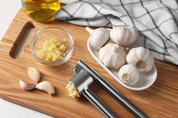 Board with metal press and crushed garlic on table, closeup