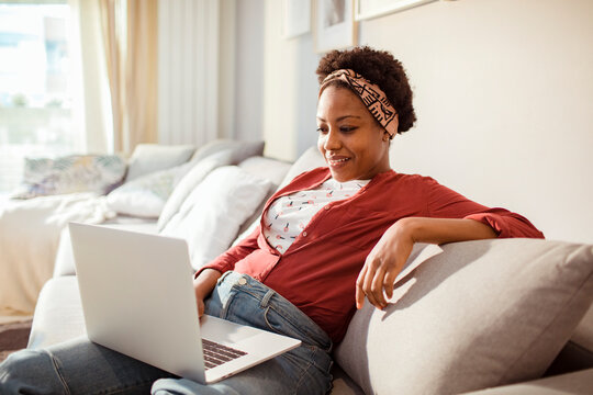 Smiling woman using laptop the couch at home