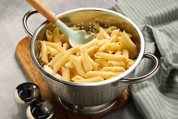 Delicious penne pasta in colander and spices on table, closeup