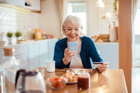 Senior woman using smartphone and credit card for online payment at home